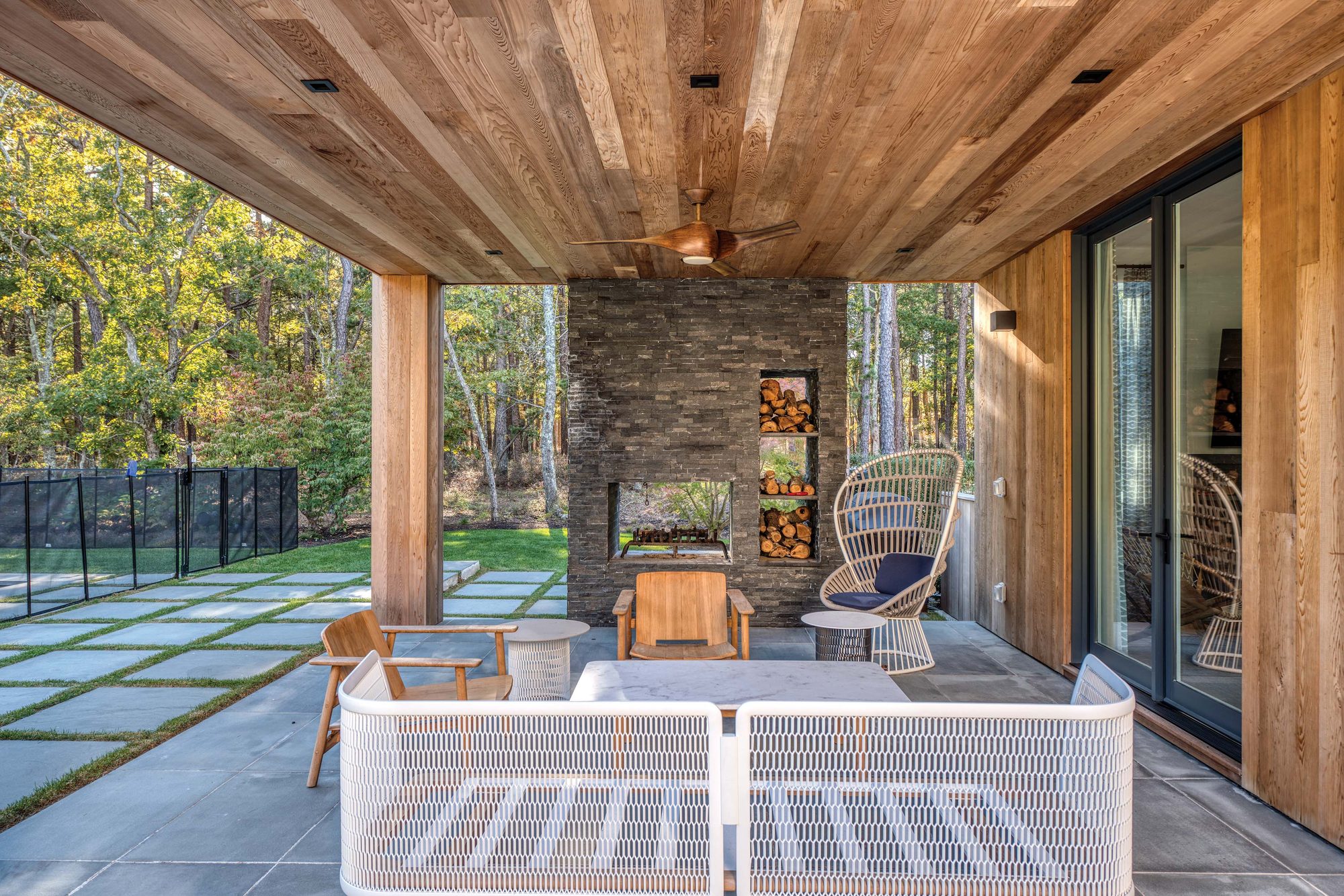 Covered porch with a cedar ceiling, stacked-stone outdoor fireplace and woven lounge chairs