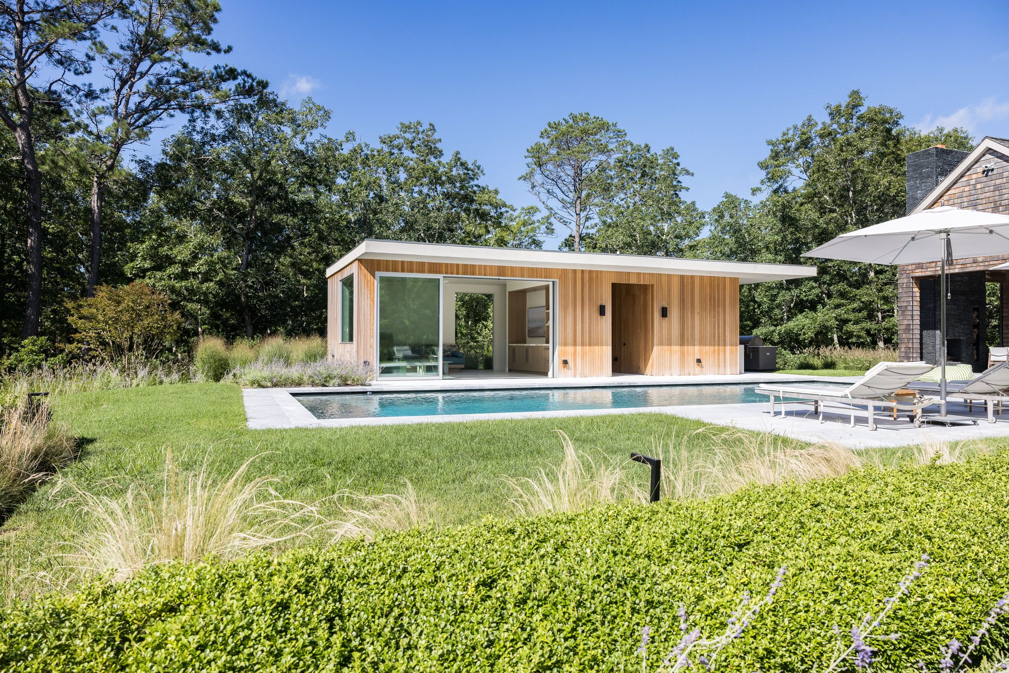 Pool and limestone terrace set in lawn and ornamental grasses, the pool house beyond