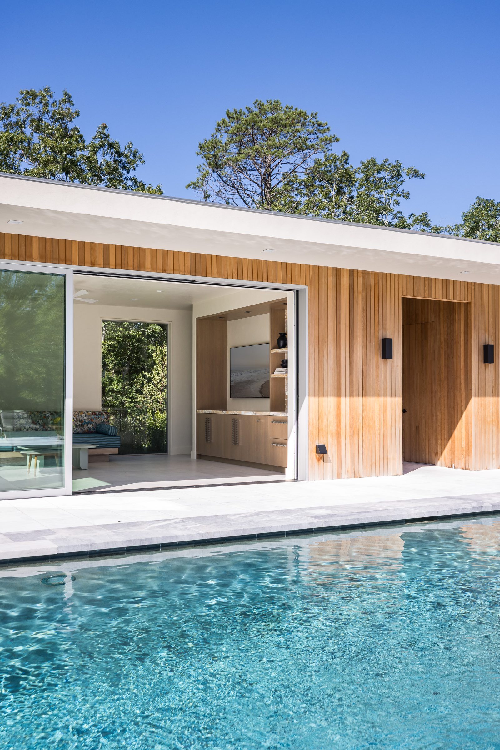 Sliding glass wall pulled back to the pool house lounge beside cedar siding