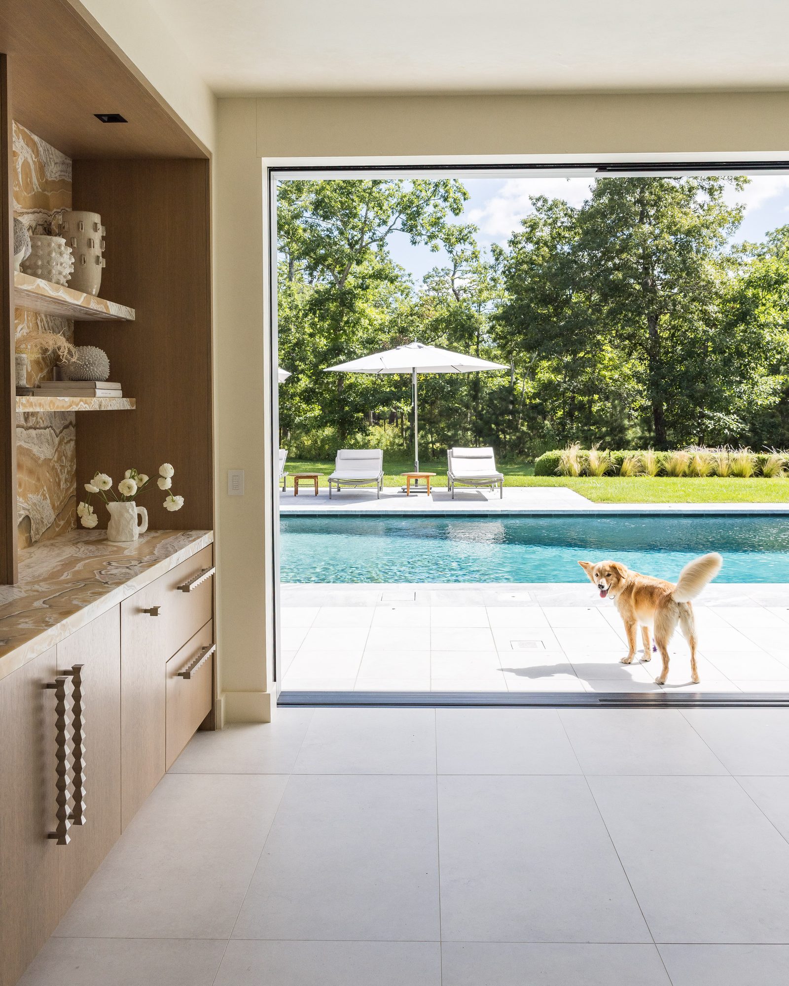 Pool house interior with oak cabinetry and stone-backed shelving, open to the pool terrace