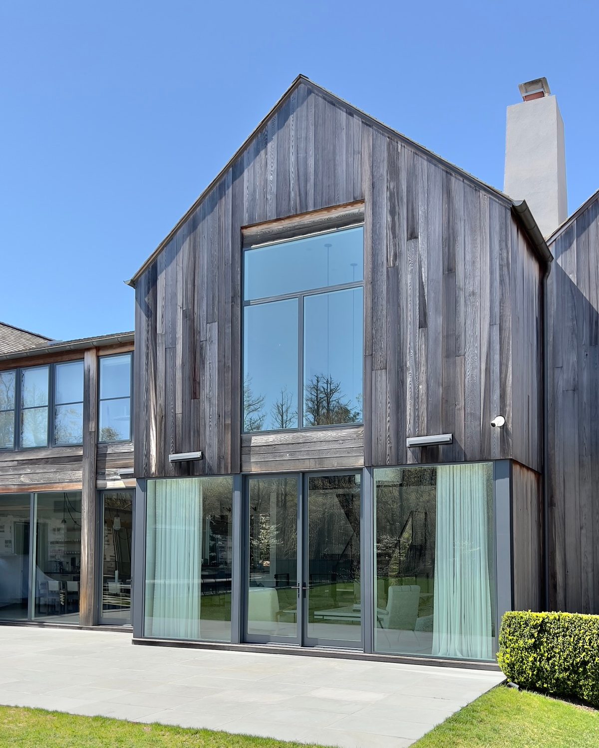 Two-story gable clad in weathered vertical cedar with floor-to-ceiling glass on the ground floor