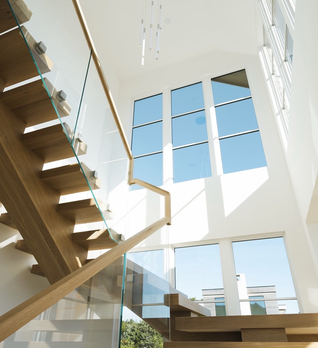 Sunlit stairwell with floating oak treads and glass rail