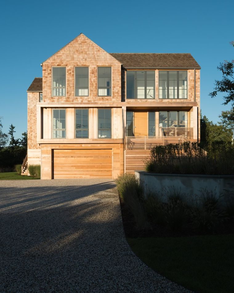Cedar-shingled two-story home and garage above dune grasses in late sun