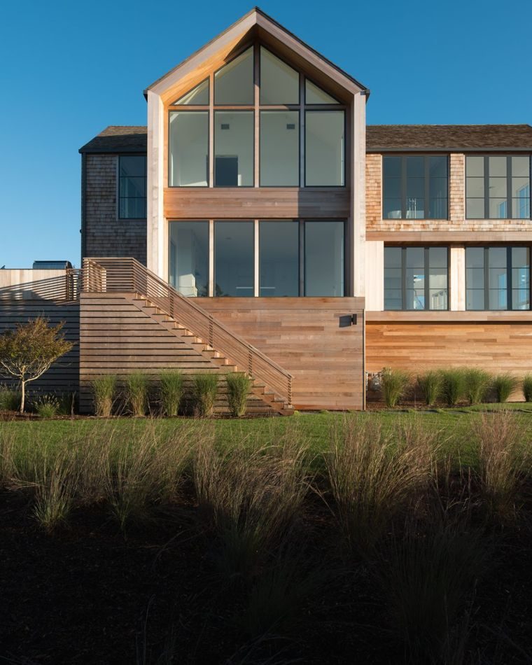 Gabled glass facade above a wide cedar stair and meadow grasses