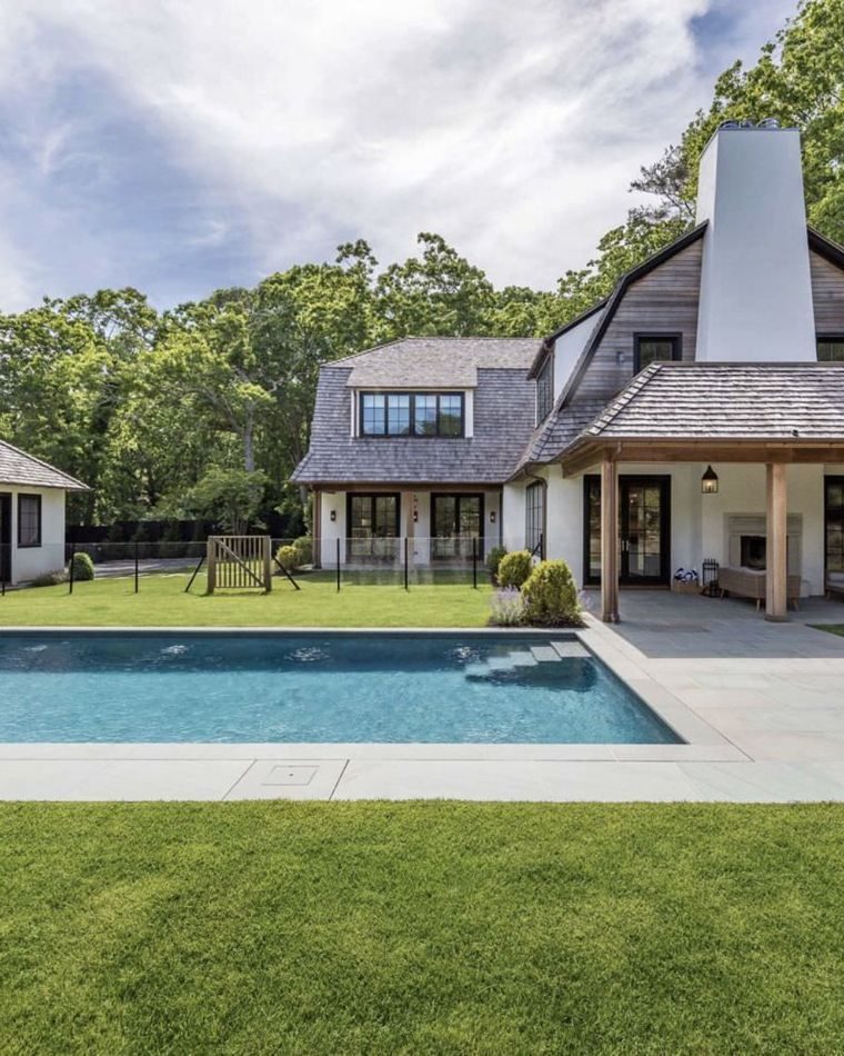 Gambrel-roofed shingle house beyond a swimming pool and lawn