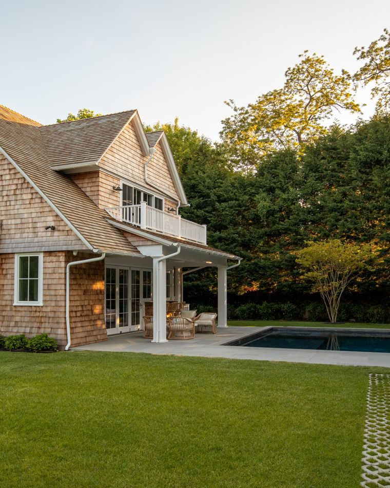 Shingled house with balcony above a pool and lawn at golden hour