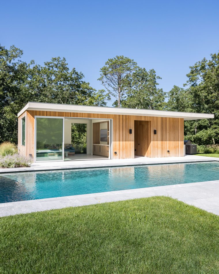 Flat-roofed cedar pool house beyond a long pool and lawn